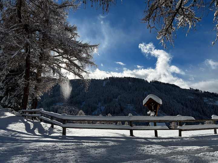Verschneiter Holzzaun und Wegkreuz am Winterwanderweg